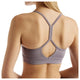 Man ser en kvinde bagfra, der har New Balance Nb Essential Yoga Bra til kvinder i farven Off-Line Grey på, udstyret med NB DRY-teknologi. Hendes lange, glatte hår falder ned over den ene skulder, og hendes hud har nogle modermærker og fregner.
