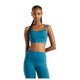 En kvinde med langt, flettet hår står foran en hvid baggrund iført New Balance Nb Essential Yoga-bh til kvinder i farven Streamsong, der er udstyret med NB DRY-teknologi, kombineret med matchende leggings med høj talje. Hendes arme hviler langs siden.