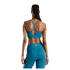 En kvinde med flettet hår poserer med ryggen til kameraet iført New Balance Nb Essential Yoga-bh til kvinder i farven Streamsong og matchende leggings med høj talje foran en hvid baggrund.