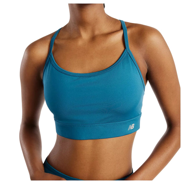 En kvinde har New Balance Nb Essential Yoga Bra, Dame i farven Streamsong på – i farven teal med tynde stropper og et lille logo nederst til venstre. Det beskårne billede fremhæver overkroppen og viser, at modellen er behagelig at have på, både til yoga og til hverdagsbrug.
