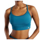 En kvinde har New Balance Nb Essential Yoga Bra, Dame i farven Streamsong på – i farven teal med tynde stropper og et lille logo nederst til venstre. Det beskårne billede fremhæver overkroppen og viser, at modellen er behagelig at have på, både til yoga og til hverdagsbrug.