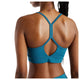 En kvinde med tre sommerfugletatoveringer på halsen og flettet hår ses set bagfra iført New Balance Nb Essential Yoga Bra, Dame, Streamsong. Denne blågrønne sports-BH med racerback er udstyret med avanceret NB DRY-teknologi til fugtregulering.