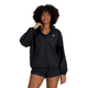 En kvinde med krøllet hår bærer en sort New Balance Athletics Packable Jacket med WATER DEFY-teknologi og sorte shorts, mens hun står på en almindelig hvid baggrund med den ene hånd på kraven.