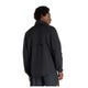 En mand med kort, krøllet hår ses bagfra iført en løstsiddende New Balance Athletics Reflective Packable Jacket i sort og mørke shorts, mens han står på en almindelig hvid baggrund.