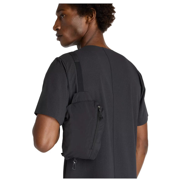 En person i en struktureret, kortærmet sort skjorte bærer en lille sort crossbody-taske og vender sig om på siden, så den ligner New Balance Athletics Reflective Packable Jacket for Men in Black set bagfra.