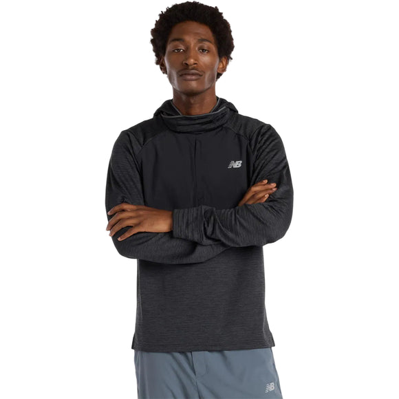En mand iført en sort New Balance Heat Grid Balaclava Hoodie til mænd med NB HEAT-teknologi og et diskret logo på venstre bryst står med armene over kors og ser frem for sig, sammen med lysegrå shorts.