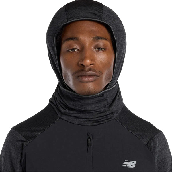 En mand iført New Balance Heat Grid Balaclava Hoodie, Herre, Black, med NB HEAT-teknologi og NB-logo på brystet, kigger ind i kameraet med et neutralt udtryk.