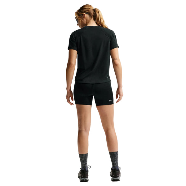 En kvinde med hestehale, set bagfra mod en hvid baggrund, er iført sorte Nike ACG High-Waisted 4" Running Shorts (Dame, Black/Summit White), en sort t-shirt, grå sokker og sorte sportssko.