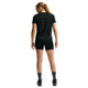 En kvinde med hestehale, set bagfra mod en hvid baggrund, er iført sorte Nike ACG High-Waisted 4" Running Shorts (Dame, Black/Summit White), en sort t-shirt, grå sokker og sorte sportssko.