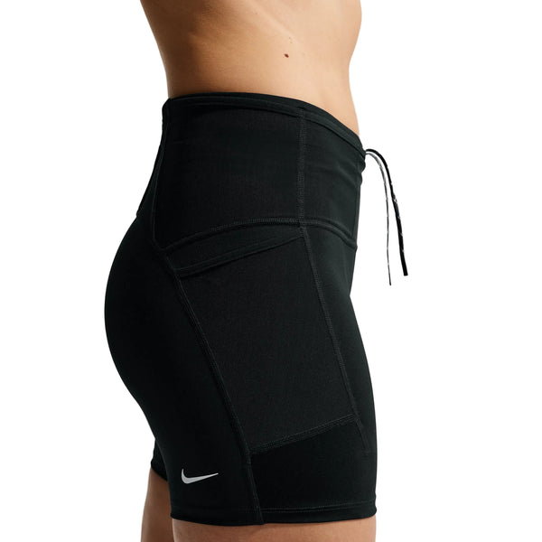 En kvinde ses fra taljen til midt på låret iført Nike ACG High-Waisted 4" løbeshorts i Black/Summit White med en synlig sidelomme og Nike-logoet på en almindelig hvid baggrund.
