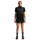En person står med front mod en sort vest med lynlås, Nike ACG Mid-Rise Brief-Lined Running Shorts til kvinder i Black/Black/Summit White, en sort kortærmet skjorte, sorte sokker og sorte sportssko på en almindelig hvid baggrund.