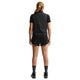 En person med langt tilbagestrøget hår, set bagfra, er iført en sort kortærmet skjorte, sort vest, Nike ACG Mid-Rise Brief-Lined Running Shorts (Dame, Black/Black/Summit White), sorte sokker og sorte sportssko på en hvid baggrund.