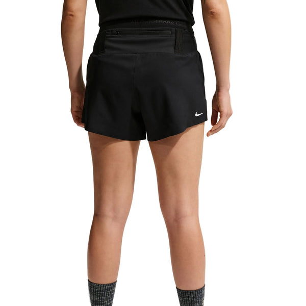 En person ses fra taljen og ned, med ansigtet vendt væk, iført Nike ACG Mid-Rise Brief-Lined Running Shorts til kvinder i Black/Black/Summit White med et lille hvidt logo, sammen med en sort top og sokker. Dri-FIT-materialet giver træningskomfort.