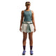 En person står med ansigtet vendt fremad og er iført en grøn tanktop og Nike ACG Mid-Rise Brief-Lined løbeshorts til kvinder i farvekombinationen Sea Glass/Sea Glass/Summit White, med en langærmet trøje bundet om taljen, mørke strømper, løbesko, en kasket og solbriller. Baggrunden er ensfarvet hvid.