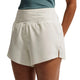 En person iført Nike ACG Mid-Rise løbeshorts med underbukser til kvinder i farvekombinationen Sea Glass/Sea Glass/Summit White, med et diskret logo på venstre ben. Personens hånd hviler på hoften, og kun den nedre del af overkroppen og lårene er synlige.