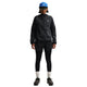 En person iført Nike ACG Repel Running Jacket til kvinder i Black/White/Summit White, sorte shorts over sorte leggings, hvide strømper, sorte sneakers, en blå kasket og sorte solbriller står på en hvid baggrund.