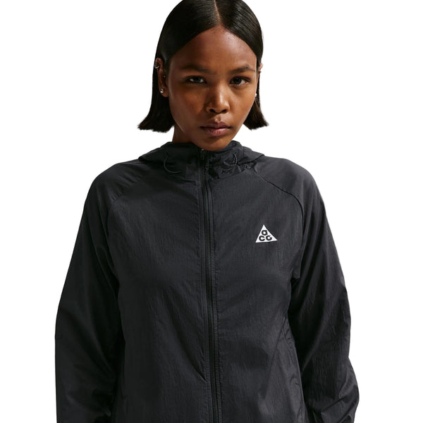 En kvinde med kort, glat hår er iført en sort Nike ACG Repel Running Jacket (Black/White/Summit White) med et lille trekantet logo på brystet og står på en hvid baggrund.
