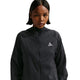 En kvinde med kort, glat hår er iført en sort Nike ACG Repel Running Jacket (Black/White/Summit White) med et lille trekantet logo på brystet og står på en hvid baggrund.