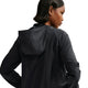 En kvinde med kort, glat hår ses bagfra iført Nike ACG Repel Running Jacket til kvinder i Black/White/Summit White. Hun kigger mod højre med venstre hånd på hoften mod en hvid baggrund.