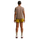 En person kigger væk fra kameraet i en Nike ACG kortærmet løbetop til kvinder, Mink Brown/Summit White, sammen med gule shorts, lyse strømper og hvide sko - ideelt til trailløb. Baggrunden er hvid.