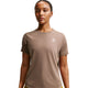 En kvinde er iført Nike ACG Short-Sleeve Running Top i Mink Brown/Summit White med et lille hvidt logo på venstre bryst og Dri-FIT-teknologi - ideel til trailløb eller hverdagskomfort - på en almindelig hvid baggrund.