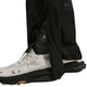 Nærbillede af en person iført hvide Nike-sneakers med sorte såler, strømper med sort og hvidt ACG-logo og Nike ACG Trailwind Waterproof Pants til mænd i Black/Summit White.