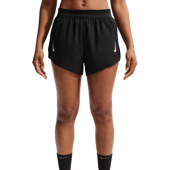 En kvinde er iført sorte Nk Arswft Dfadv 3In Short 26 fra Nike med hvide logoer på hvert ben. Hun står med afslappede arme, hvor overkrop og ben vises delvist, hvilket fremhæver det åndbare løbeshorts-design.