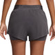 En person ses fra taljen og ned iført Nike Dri-FIT Mid-Rise 2-i-1 løbeshorts til kvinder i Thunder Grey/Reflective Silver. Bagsiden fremhæver pasformen, det lagdelte design og materialet i disse alsidige dame løbeshorts.
