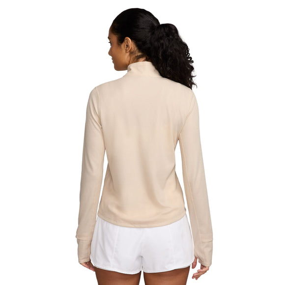 En kvinde med langt mørkt hår i hestehale står med ryggen til kameraet iført Nike Dri-FIT Trail 1/2-Zip Mid Layer til kvinder i Pearl White/Summit White og hvide shorts på en almindelig hvid baggrund.