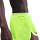 Et nærbillede fra siden viser en person iført Nike Dri-FIT ADV 4" Brief-Lined Running Shorts til mænd i Volt/Black med avanceret fugttransporterende teknologi og en synlig Nike Swoosh på venstre side mod en hvid baggrund.