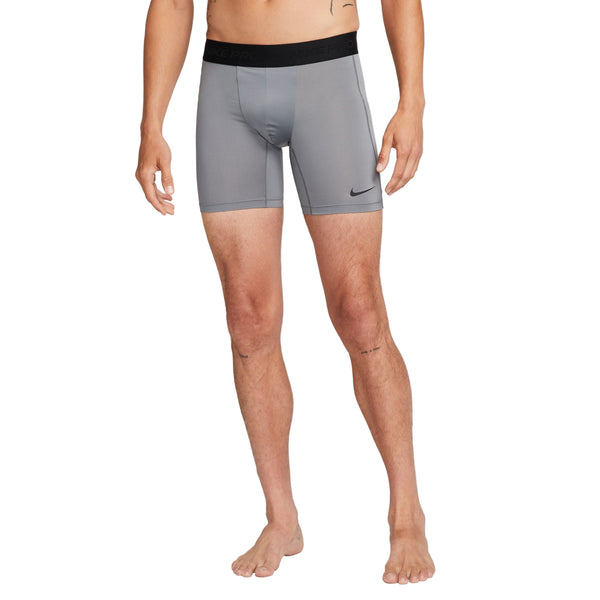 En person står barfodet med front mod en hvid baggrund iført Nike Dri-FIT Fitness Shorts til mænd i Smoke Grey/Black.