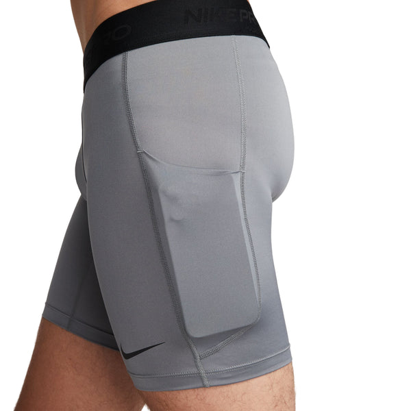Et nærbillede fra siden viser en person iført Nike Dri-FIT Fitness Shorts, Herre, Smoke Grey/Black med sort linning og en stor lårlomme. Nike-logoet nær kanten fremhæver shortsens slanke, atletiske design.