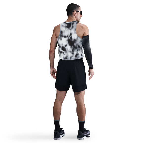 En mand kigger væk mod en hvid baggrund iført Nike Dri-Fit Adv Running Tank Top til mænd i Black/Black/Reflective Silver, sammen med sorte shorts, solbriller og et sortmønstret ærme på venstre arm.