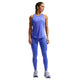 En kvinde står med ansigtet fremad i Nike Nk Df Swift Hr 7/8 Tight, Dame, Sapphire/Reflective Silv leggings og en blå ærmeløs top med hvide sneakers. Hendes flettede hår og blik til siden viser det stilfulde løbetights dame-look på en hvid baggrund.