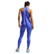 En person med flettet hår står og kigger væk, iført en ærmeløs lilla sportstop, Nike Nk Df Swift Hr 7/8 Tight leggings (Sapphire/Reflective Silv) og lyseblå og hvide sneakers på en hvid baggrund.