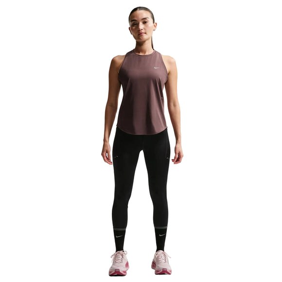 En kvinde står med ansigtet fremad i en brun Nike Nk Swift Df Tank Top, Dame, Tattoo/Reflective Silv med sorte leggings og pink løbesko. Denne Nike-top er åndbar og perfekt til træning. Baggrunden er helt hvid.