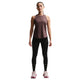En kvinde står med ansigtet fremad i en brun Nike Nk Swift Df Tank Top, Dame, Tattoo/Reflective Silv med sorte leggings og pink løbesko. Denne Nike-top er åndbar og perfekt til træning. Baggrunden er helt hvid.
