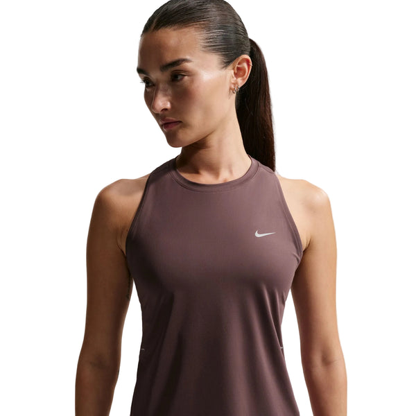 En kvinde med langt mørkt hår i hestehale bærer en Nike Nk Swift Df Tank Top, Dame, Tattoo/Reflective Silv, med et lille hvidt logo på brystet, mens hun kigger til siden mod en almindelig hvid baggrund.