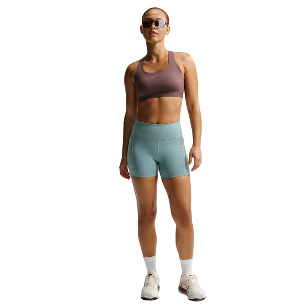 En person med solbriller, iført et Nike Nk Swift Hs Bra Dame Tattoo/Silver-trøje med Dri-FIT-teknologi, lyseblå sportsshorts, hvide sokker og hvide sneakers står foran en hvid baggrund.