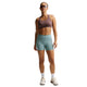 En person med solbriller, iført et Nike Nk Swift Hs Bra Dame Tattoo/Silver-trøje med Dri-FIT-teknologi, lyseblå sportsshorts, hvide sokker og hvide sneakers står foran en hvid baggrund.