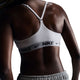 En person med mørk hud ses bagfra iført Nike Padded Adjustable Sports Bra, Dame, White/Black, med Dri-FIT-materiale, racerback-design og Nike-logo på båndet, sat sammen med lysegrå shorts.