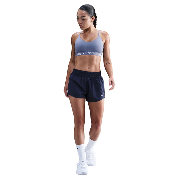 En kvinde iført en World Indigo Nike Padded Adjustable Sports Bra, marineblå sportsshorts, hvide strømper og hvide sneakers står og kigger nedad mod en hvid baggrund.