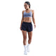En kvinde iført en World Indigo Nike Padded Adjustable Sports Bra, marineblå sportsshorts, hvide strømper og hvide sneakers står og kigger nedad mod en hvid baggrund.