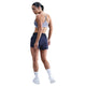 En kvinde står med ryggen til, hovedet til siden, iført en Nike Padded Adjustable Sports Bra, Dame, World Indigo, marineblå shorts, hvide strømper og hvide sportssko på en almindelig hvid baggrund.