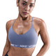 En kvinde ser frem for sig i en Nike Padded Adjustable Sports Bra, Dame, World Indigo, med sorte underbukser. Hendes våde hår er trukket tilbage, og hun er synligt svedig, hvilket tyder på en træning. Baggrunden er helt hvid.