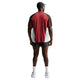 En mand står med ryggen til kameraet iført en Nike Retro SS-løbetrøje i farverne Team Crimson/Black/Reflective Silv, sorte shorts, hvide sokker og sneakers samt en sort kasket foran en ensfarvet hvid baggrund.