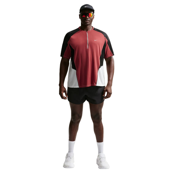 En person står med ansigtet vendt fremad iført en Nike Retro SS løbetrøje, herre, i farvekombinationen Team Crimson/sort/reflekterende sølv, kombineret med sorte shorts, hvide sokker og sneakers, en sort kasket og solbriller, foran en ensfarvet hvid baggrund.