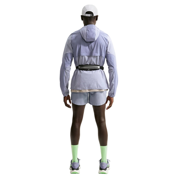 En person kigger væk og er iført en Nike Stride Plus Reple Running Jacket til mænd i Iron Purple/Indigo Haze/Reflective Silver med matchende shorts, neongrønne sokker, hvide løbesko, en hvid kasket og en sort taljetaske på en hvid baggrund.