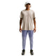 En person iført en beige t-shirt, Nike Stride Repel løbebukser til mænd i Iron Purple/Indigo Haze/Reflective, sorte sneakers, en hvid kasket og hvide hovedtelefoner står med front mod en hvid baggrund.