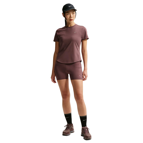 En person er iført en matchende lilla Nike Swift SS løbetop (Dame, Tattoo/Reflective Silv) og shorts, stylet med en sort kasket, strømper og lilla sneakers. Dri-FIT-materialet og de diskrete Nike-logoer fremhæver det sporty look mod en hvid baggrund.